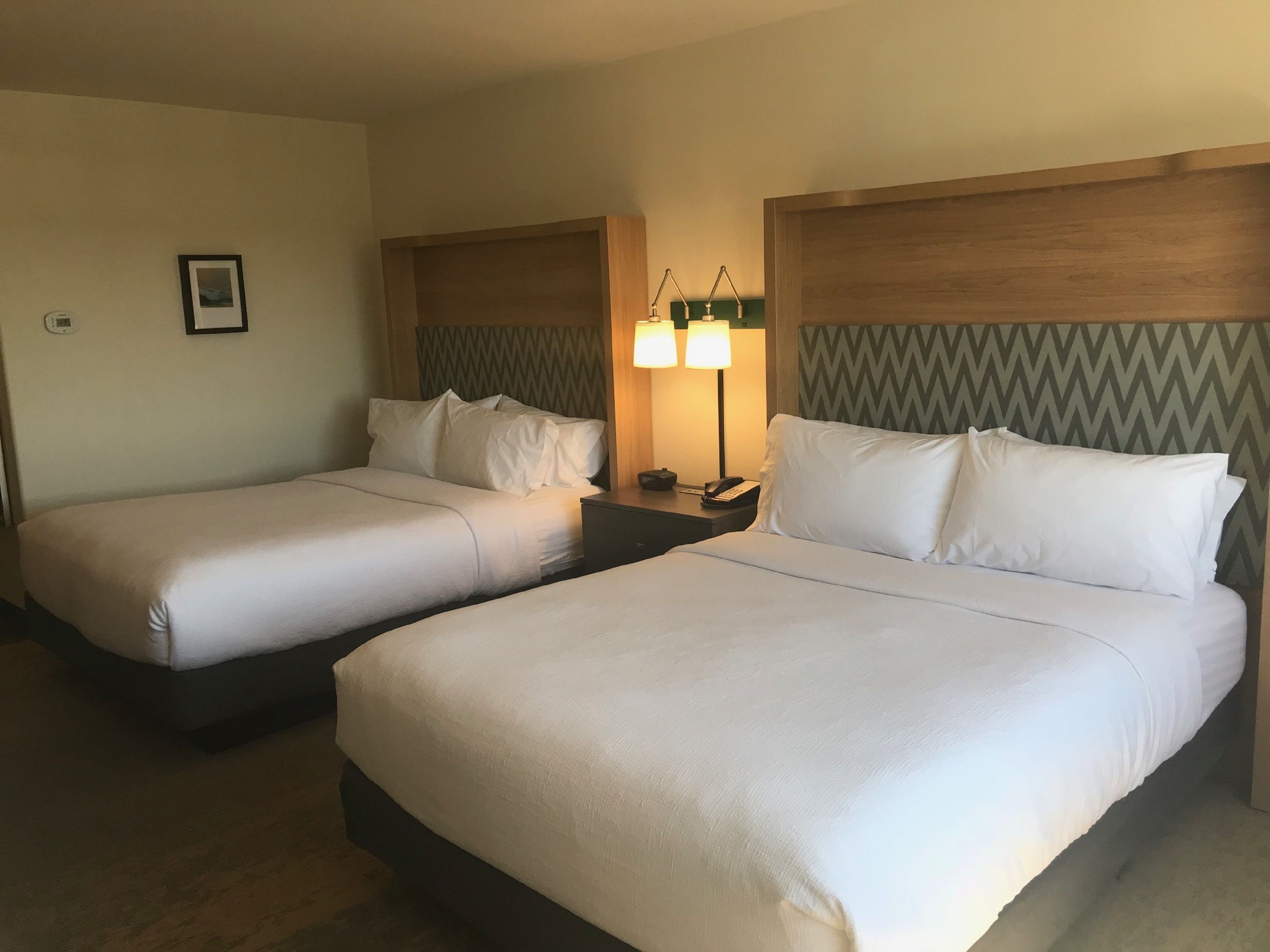 Two single beds with wooden headboards, a nightstand with a lamp, and a framed picture on the wall.