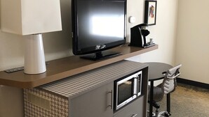Ein Hotelzimmer mit Flachbildfernseher auf einer Holzkonsole, einem Schreibtisch mit Stuhl und einer Mikrowelle.