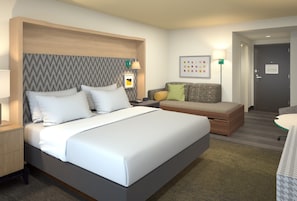 A hotel room with a large bed, a bedside table, a small sofa, a lamp, and a wall art piece.