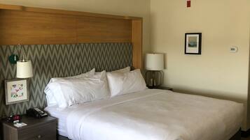 A hotel room with a bed, nightstands, a wall-mounted lamp, a framed picture, and a thermostat.