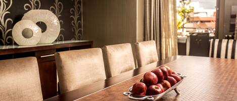 Una mesa de comedor con un bol metálico de manzanas, rodeada de sillas tapizadas.