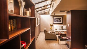 A cozy reading nook with a bookshelf, a comfortable armchair, a small table with a lamp, and a sofa.