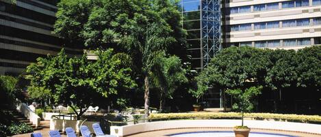 Una piscina con sillas de descanso, rodeada de vegetación y edificios modernos.