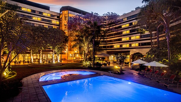 A hotel with a swimming pool, outdoor seating, and a well-lit building facade.