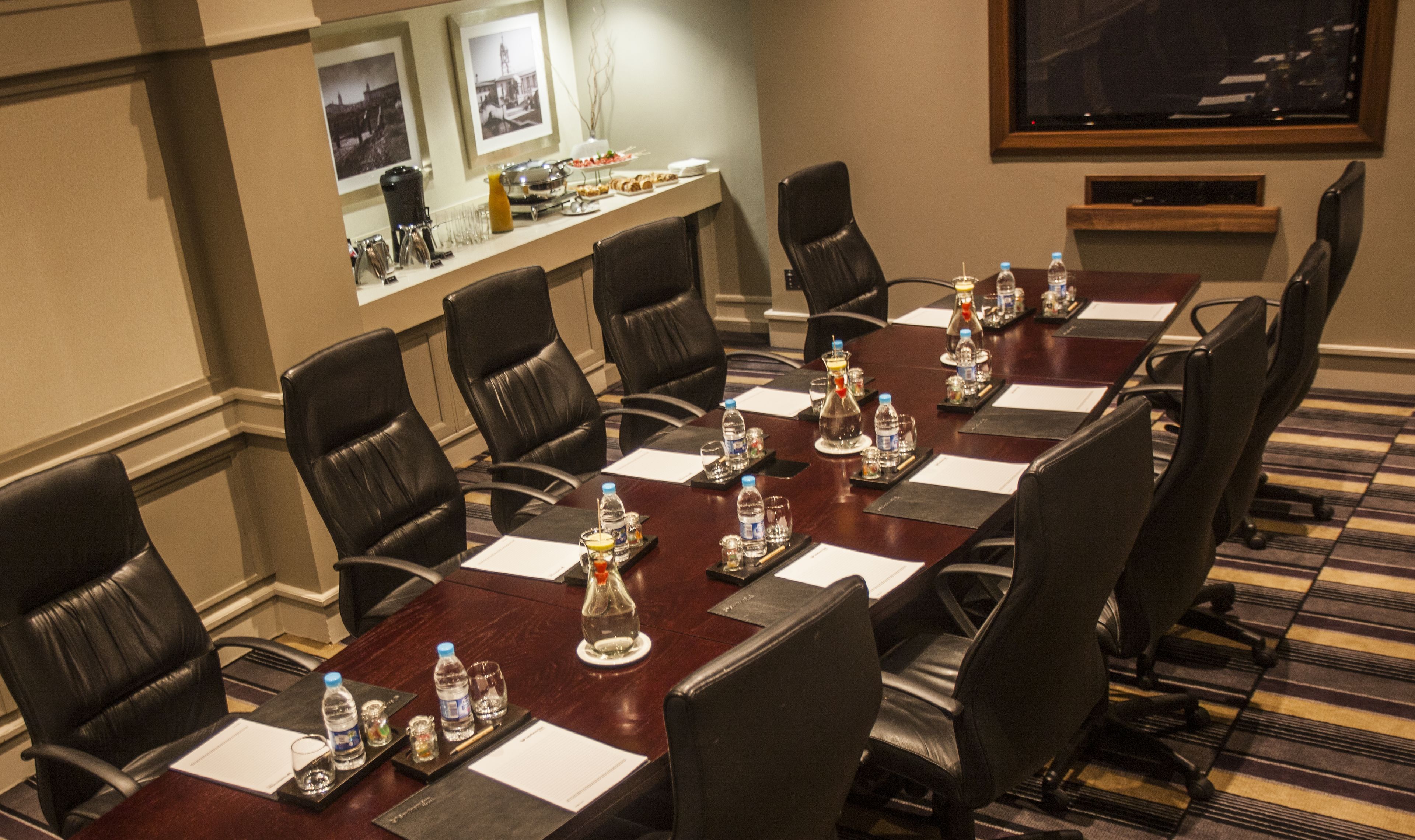 A conference room with a long table, black leather chairs, water bottles, and a coffee station.