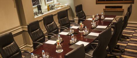 A conference room with a long table, black leather chairs, water bottles, and a coffee station.