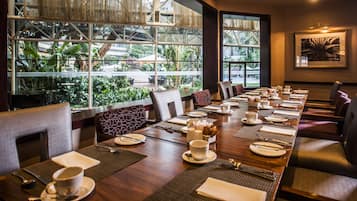 A conference room with a long table set for a meeting, large windows with a view of greenery, and a framed picture on the wall.