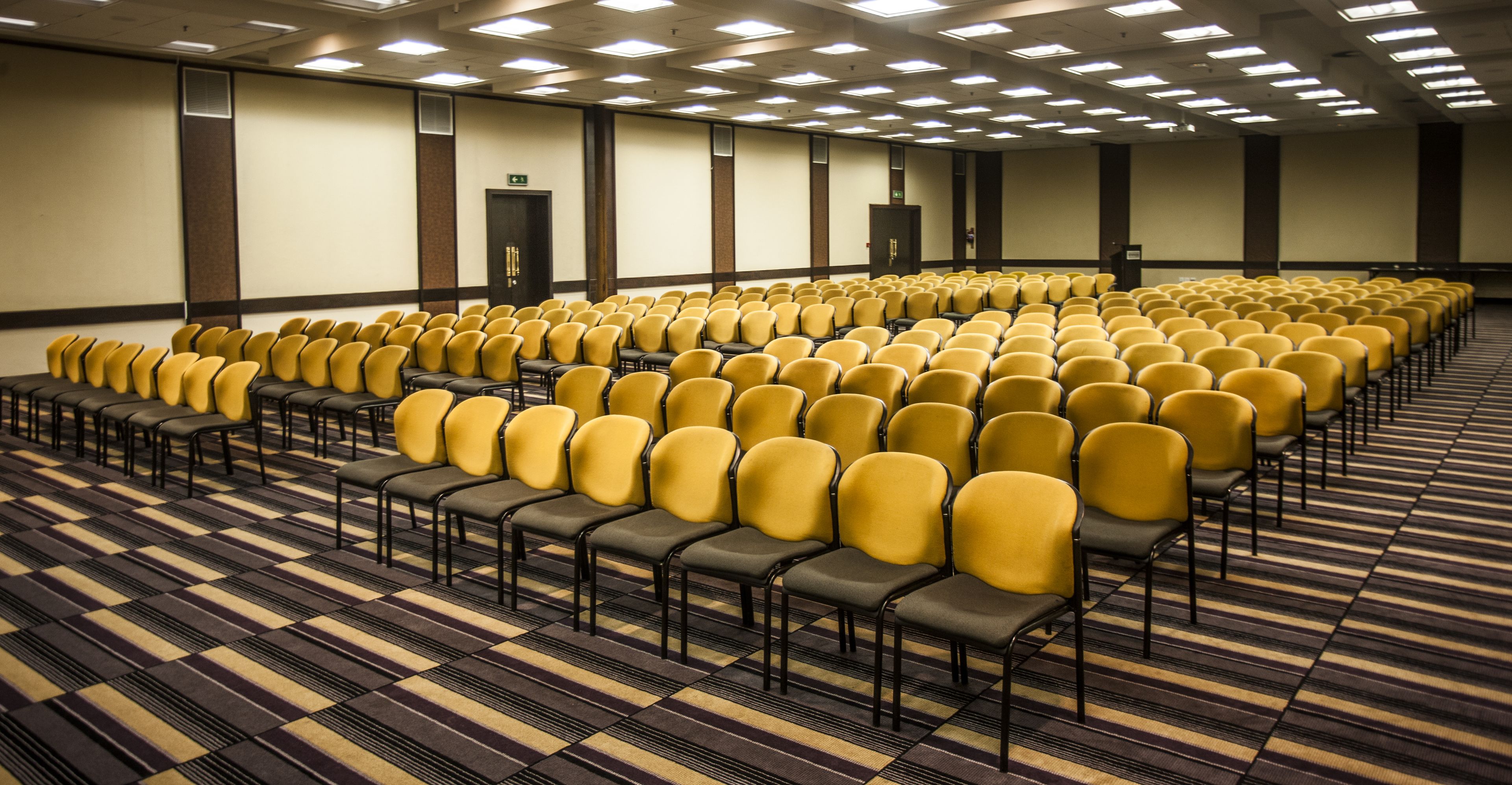 Une salle de conférence avec des rangées de chaises jaunes et un tapis à motifs.