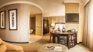 A hotel room with a curved wall, a minibar, a television, a shower, and a dining area.