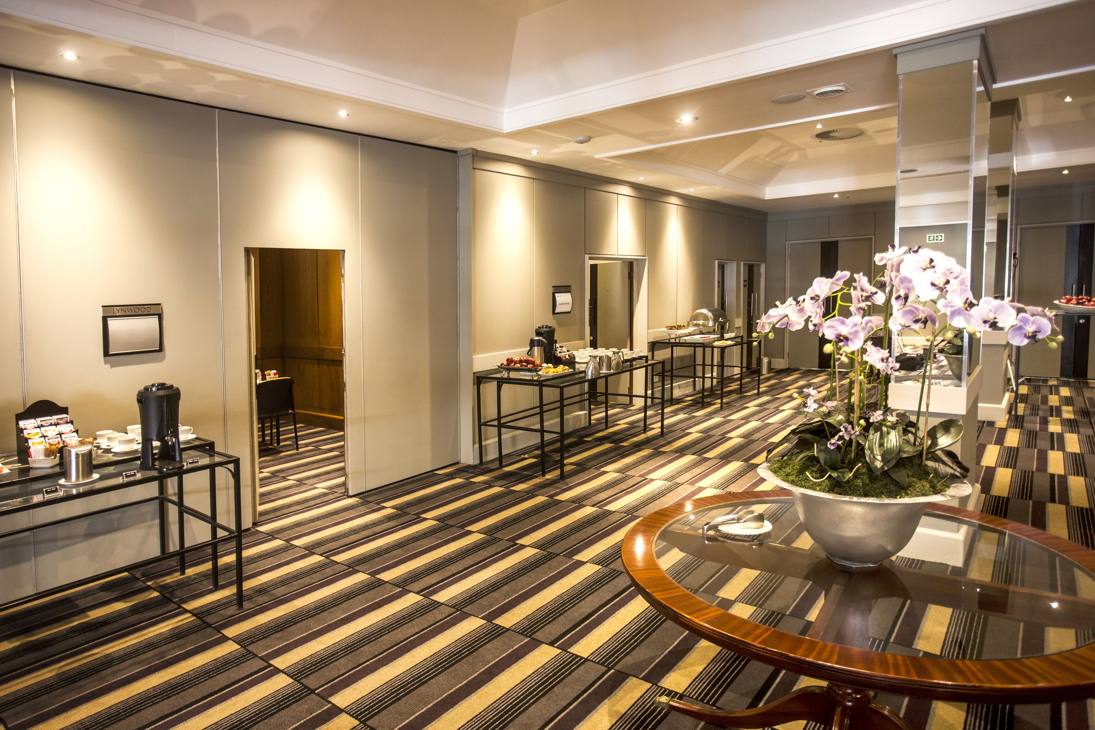 A hotel lobby with a checkered floor, a round table with a glass top, and a potted orchid plant.