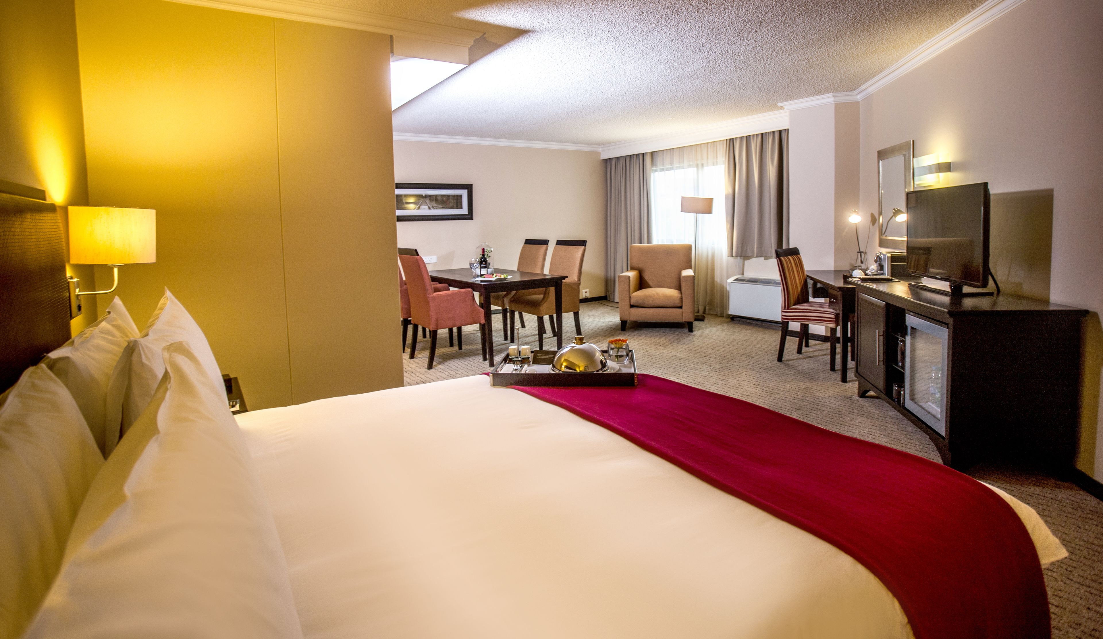 A hotel room with a large bed, a desk with a chair, a television, and a minibar.
