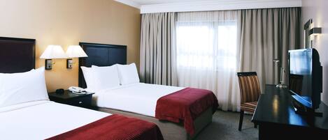 A hotel room with two beds, a desk with a TV, a chair, and a lamp.