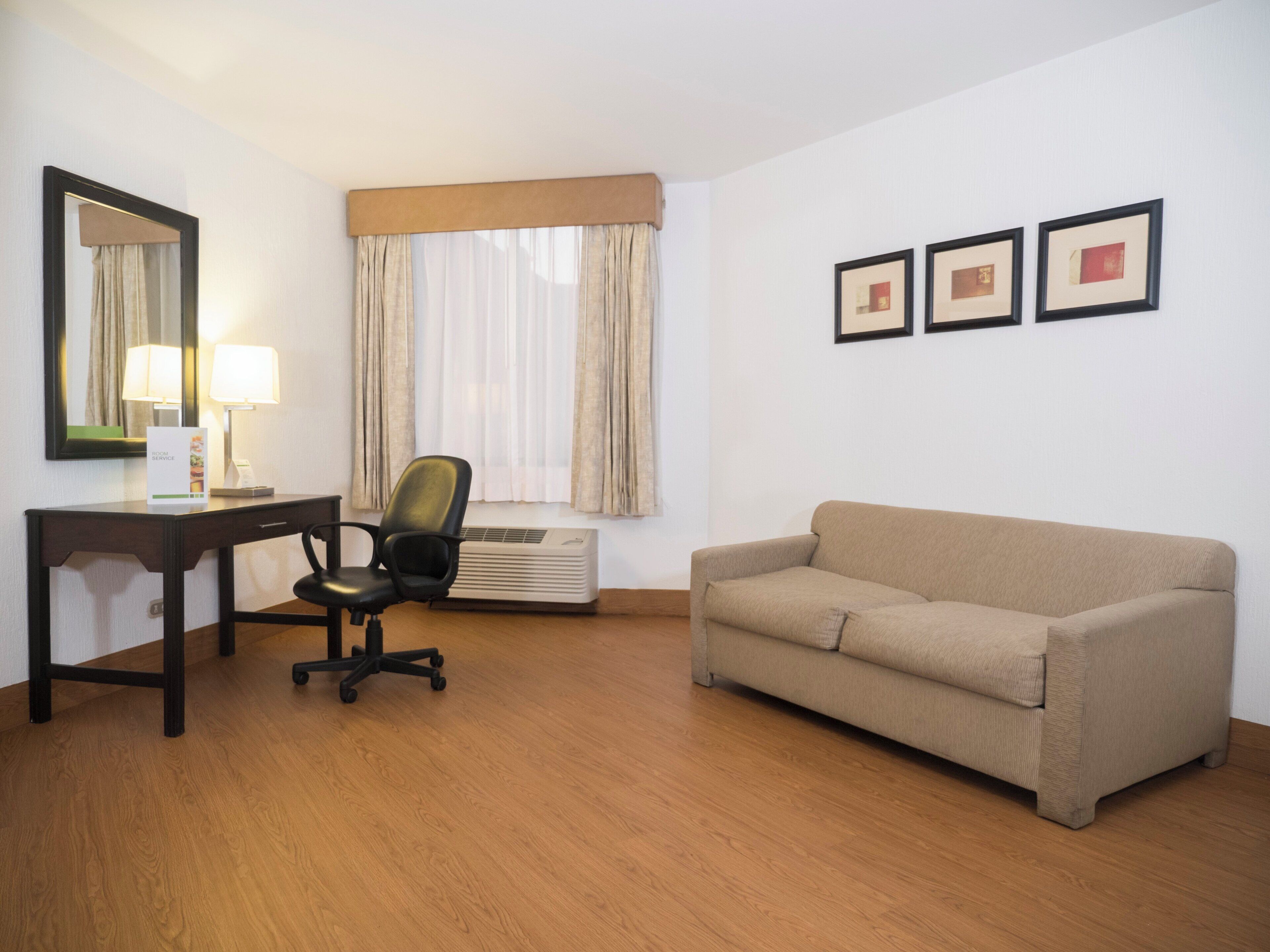 Une chambre d’hôtel équipée d’un bureau, d’une chaise, d’un canapé et d’une fenêtre avec des rideaux.