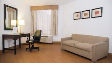 Une chambre d’hôtel équipée d’un bureau, d’une chaise, d’un canapé et d’une fenêtre avec des rideaux.