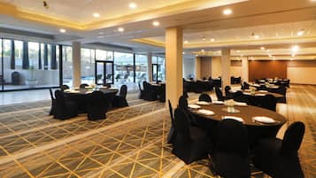 A spacious conference room with multiple round tables, black chairs, and a patterned carpet.