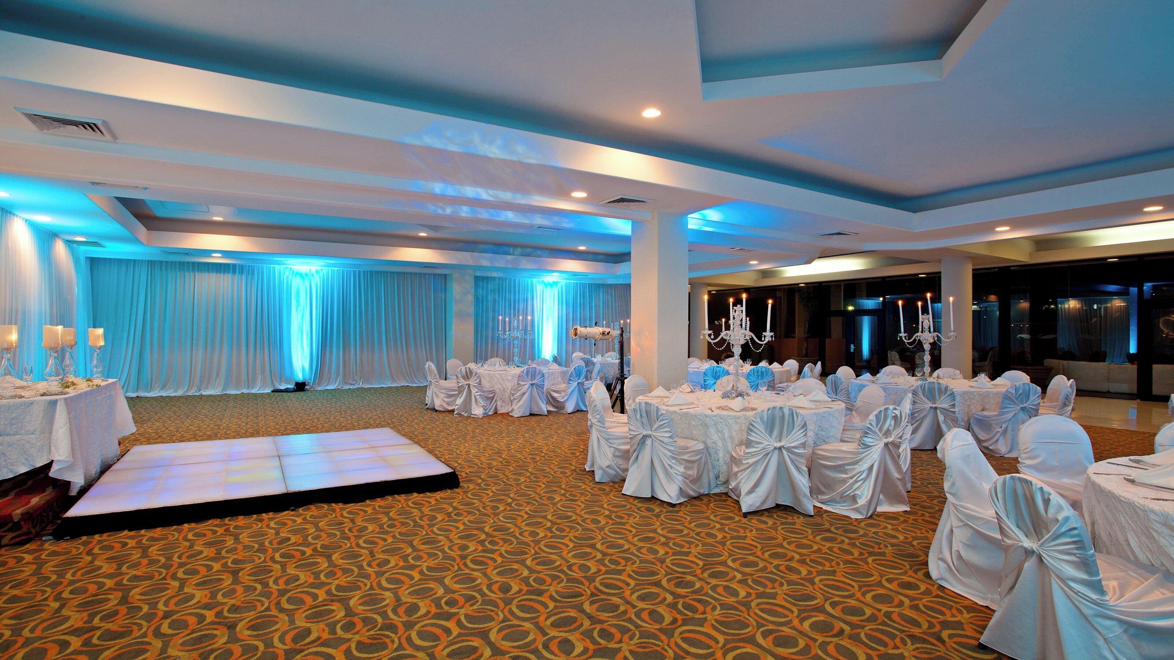 Un salón de banquetes con mesas redondas, sillas y una zona escenario.