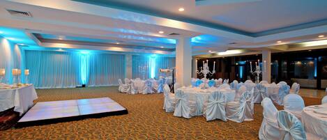 Un salón de banquetes con mesas redondas, sillas y una zona escenario.