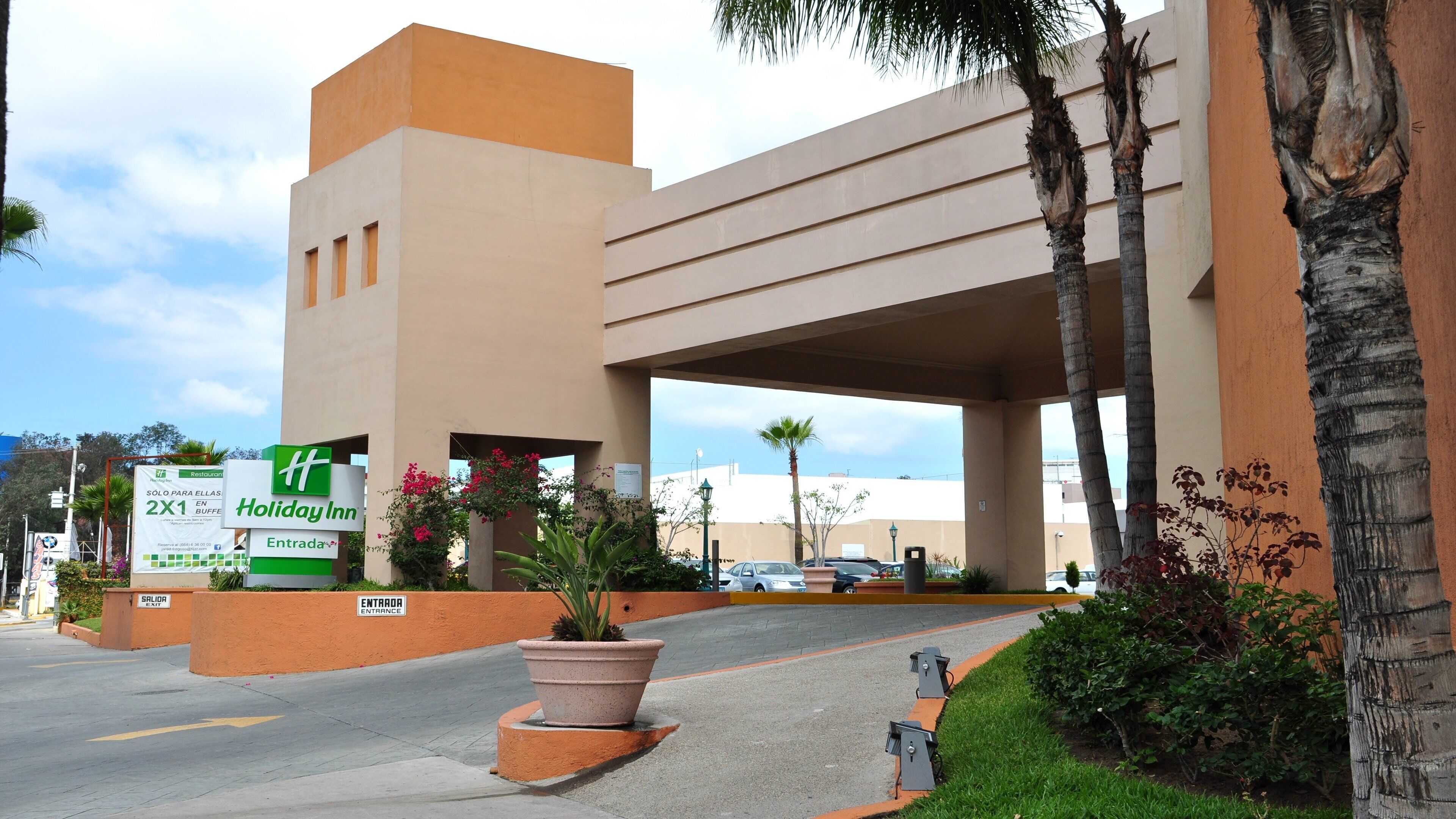 A hotel entrance with a sign for Holiday Inn, a parking area, and a clear sky.