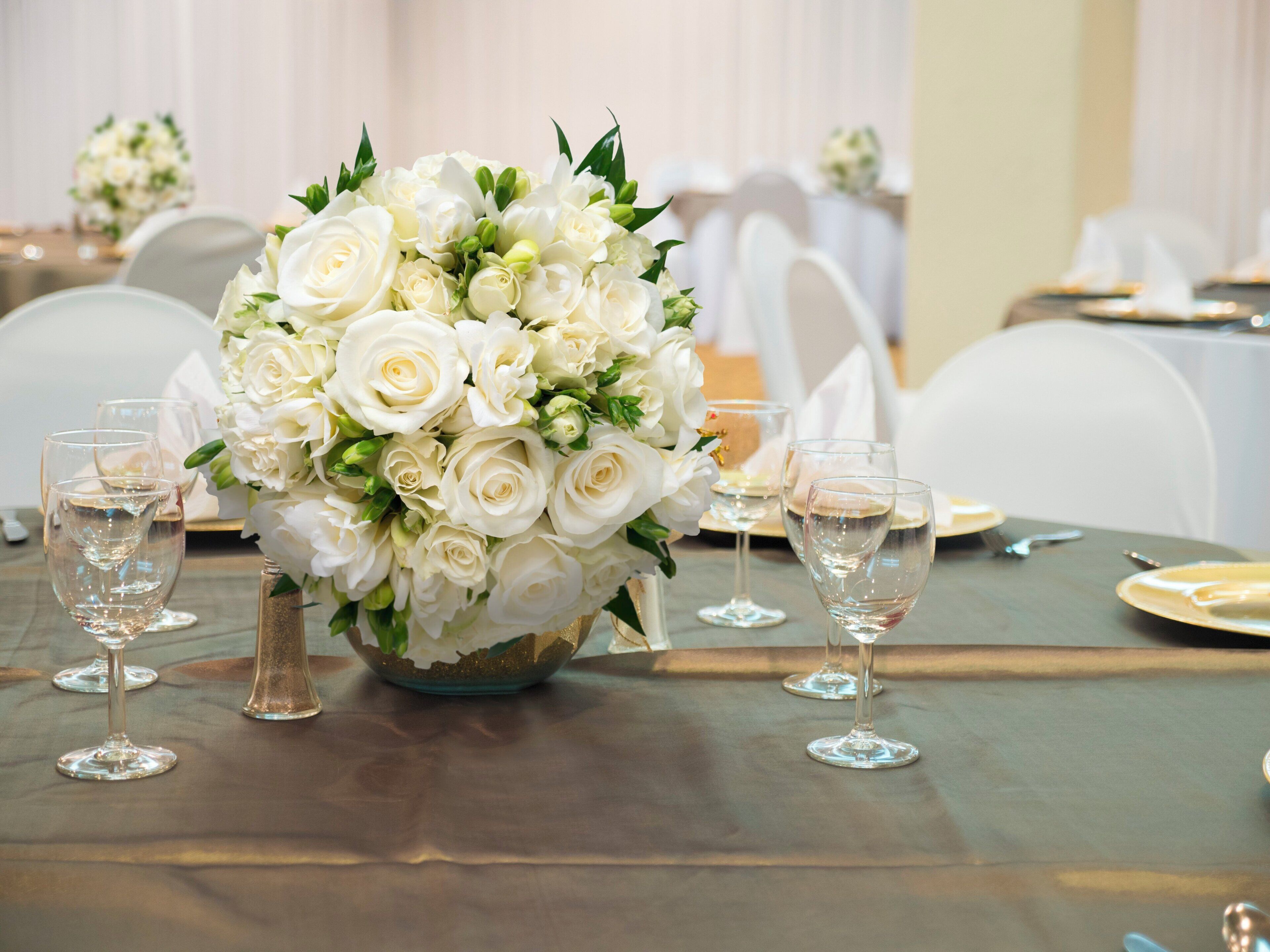 Een gedekte tafel voor een formeel evenement, met een bloemstuk van witte bloemen, glazen servies en een bord met gouden rand.