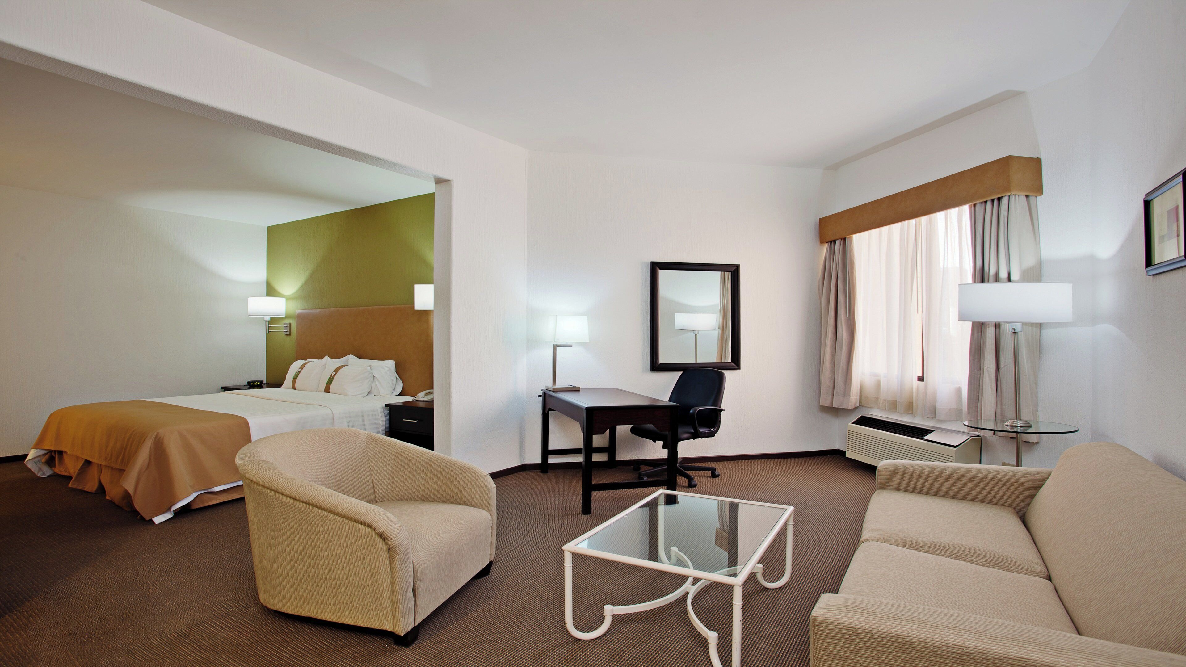 A hotel room with a bed, two armchairs, a desk, and a glass coffee table.
