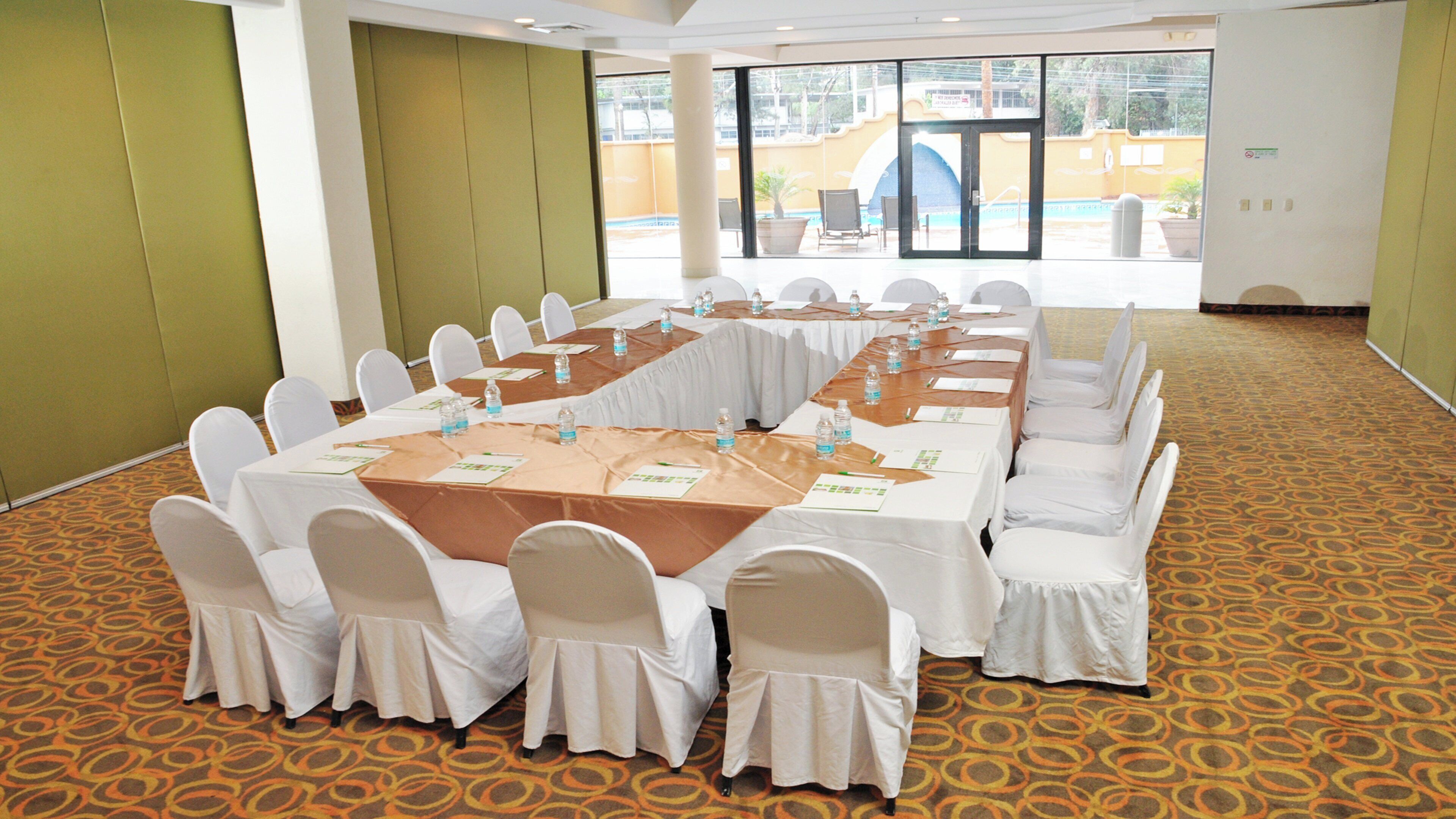 A conference room with a long table, white chairs, and a carpeted floor.