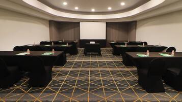 A conference room with a large screen, tables with chairs, and water bottles.