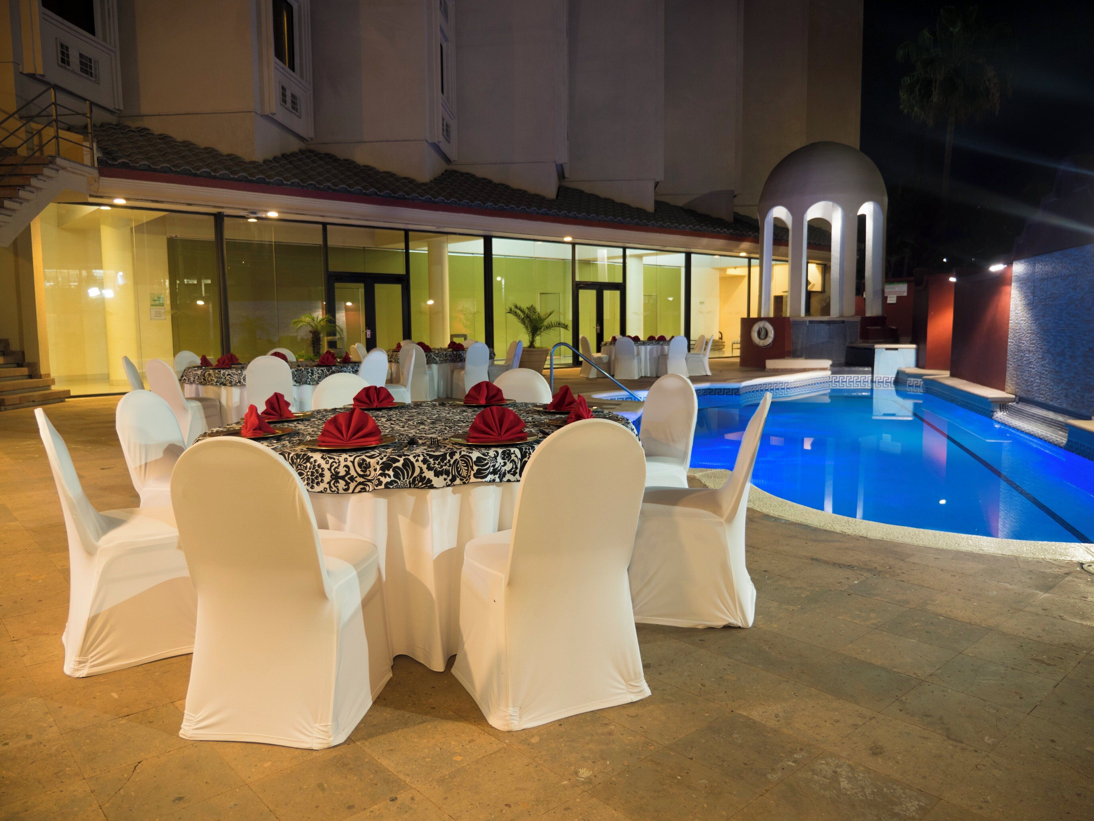 A poolside dining area with tables set for an event, a pool, and a building with a dome structure.