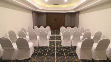 Uma sala de conferências com fileiras de cadeiras brancas, um tapete estampado e uma parede de painéis de madeira.