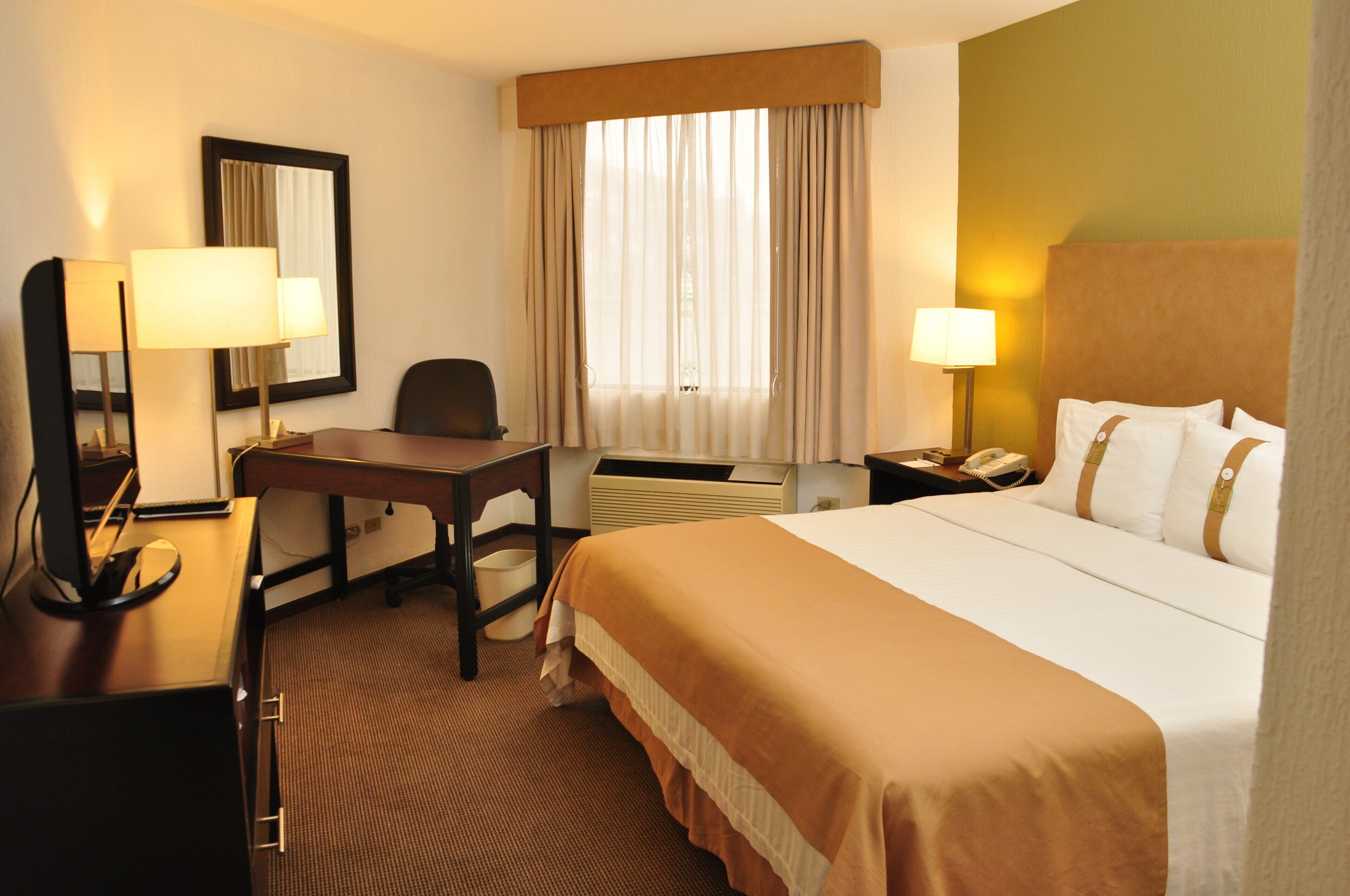 Une chambre d’hôtel équipée d’un lit, d’un bureau, d’une chaise, de lampes et d’un téléphone.