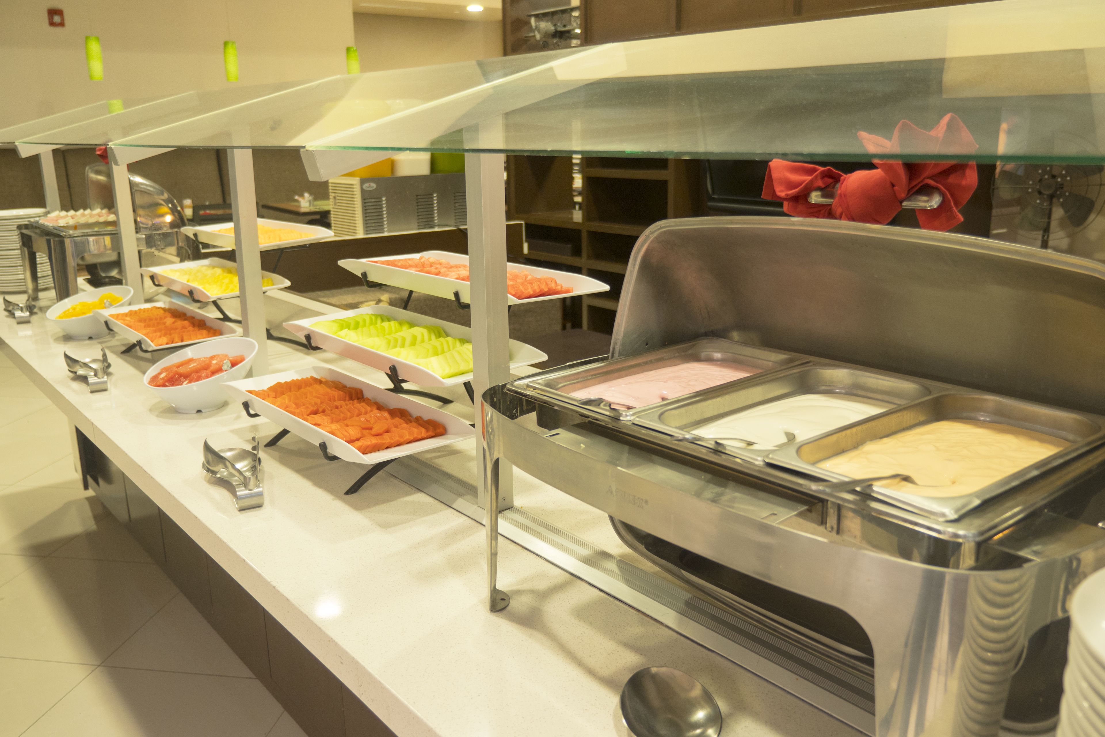 Un buffet proposant une variété de plats présentés dans des récipients séparés, disposés sur un long comptoir surmonté d’une vitre.
