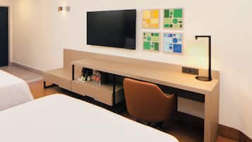 A hotel room with a bed, a desk with a chair, a flat-screen TV, and artwork on the wall.
