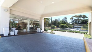 A spacious entrance area with a tiled floor, potted plants, and a view of the street and trees.