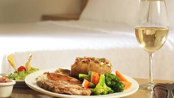 A plate of food including steak, vegetables, and a baked potato, with a glass of white wine on a table.