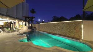 An outdoor swimming pool with a tiled edge, surrounded by lounge chairs and a pergola.