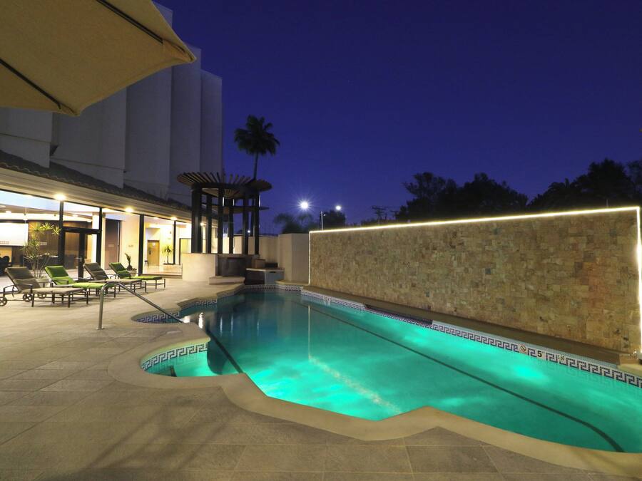 An outdoor swimming pool with a tiled edge, surrounded by lounge chairs and a pergola.