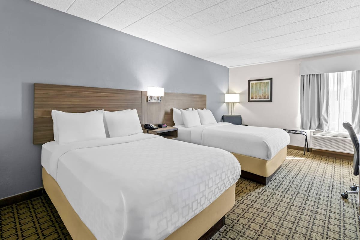 A hotel room with two beds, a desk, a chair, a lamp, and a painting on the wall.