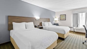A hotel room with two beds, a desk, a chair, a lamp, and a painting on the wall.