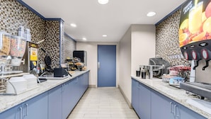 Un espace cuisine moderne avec une porte bleue, une machine à café et un distributeur de jus de fruits.