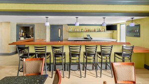 Un espace bar avec un long comptoir, de nombreuses chaises et une cuisine à l’arrière-plan.