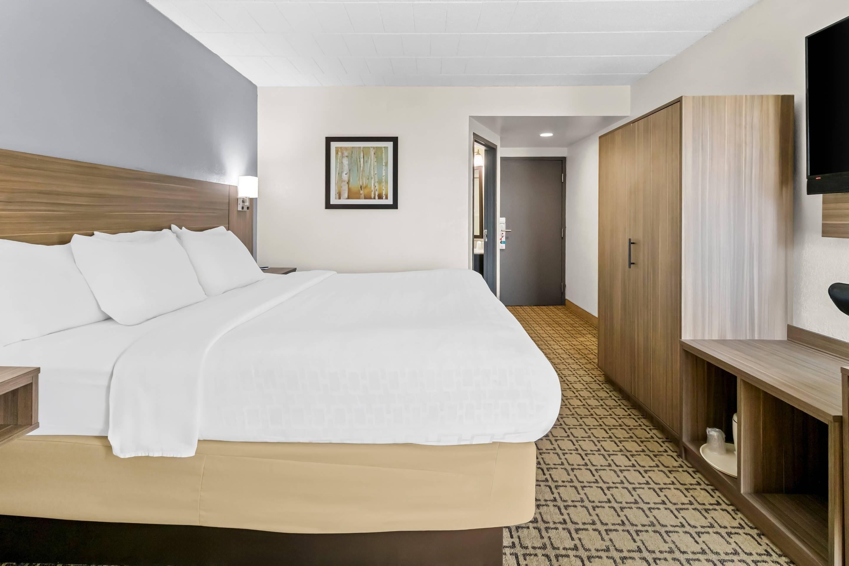 A hotel room with a large bed, a wooden wardrobe, a television, and a framed picture on the wall.
