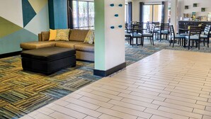 A hotel lobby with a sectional sofa, ottoman, and a dining area with chairs and tables. - Quality Inn Thornburg (Woodford)