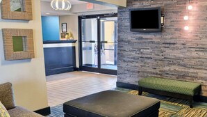 A lobby with a sofa, ottoman, patterned cushions, a bench, a flat-screen TV, and a stone wall. - Quality Inn Thornburg (Woodford)