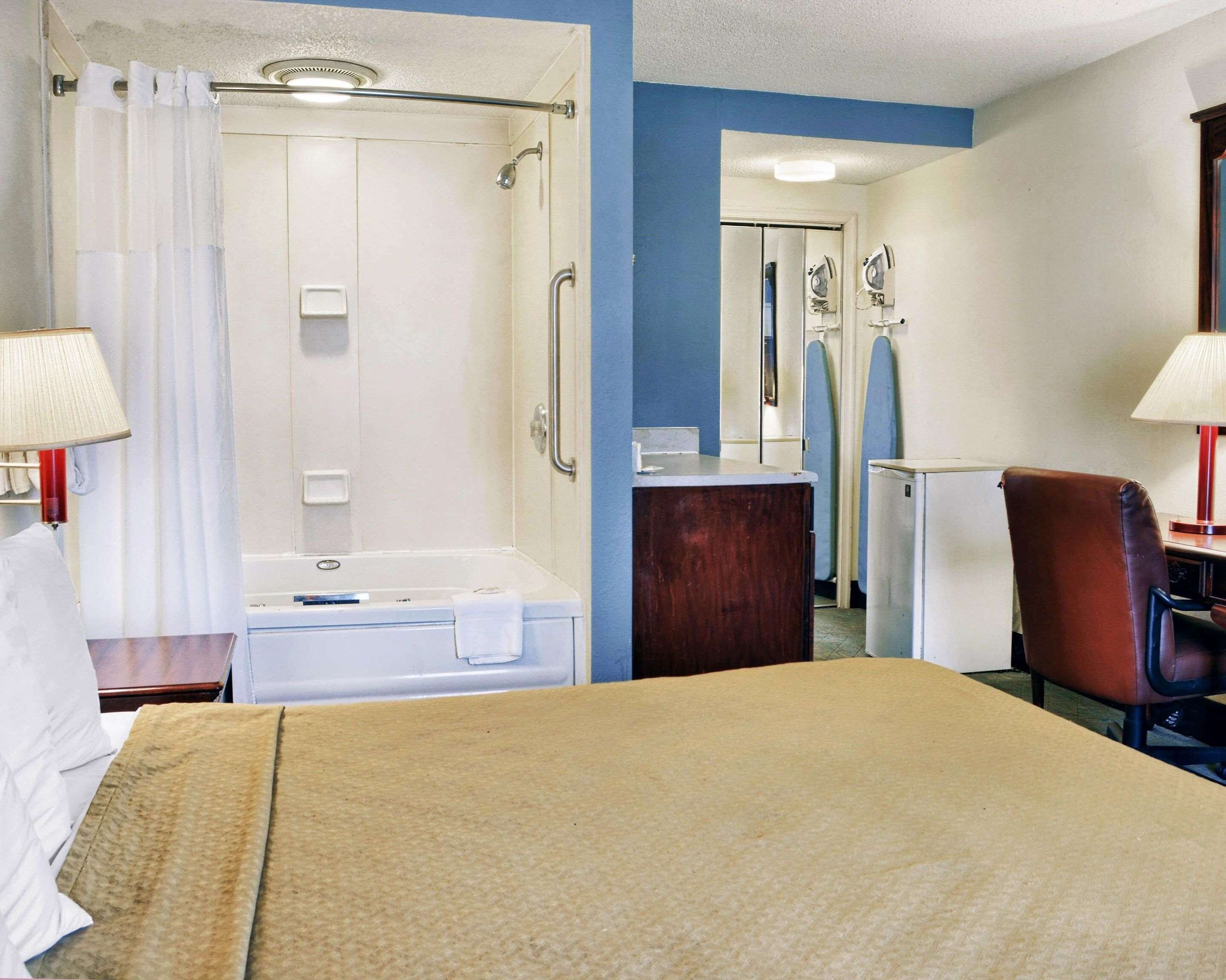 Ein Hotelzimmer mit Bett, Dusche, Schreibtisch, Stuhl und Lampe.