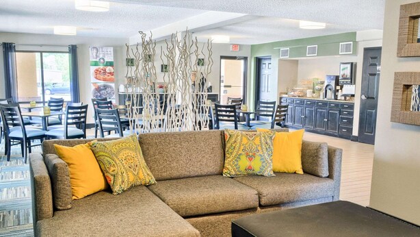 A sectional sofa with patterned cushions, a black ottoman, and a decorative white wall piece in a hotel lobby. - Quality Inn Thornburg (Woodford)