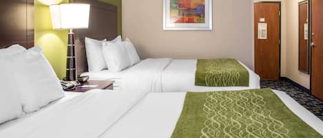 A hotel room with two beds, a bedside table with a lamp, a framed artwork on the wall, and a door with a sign.