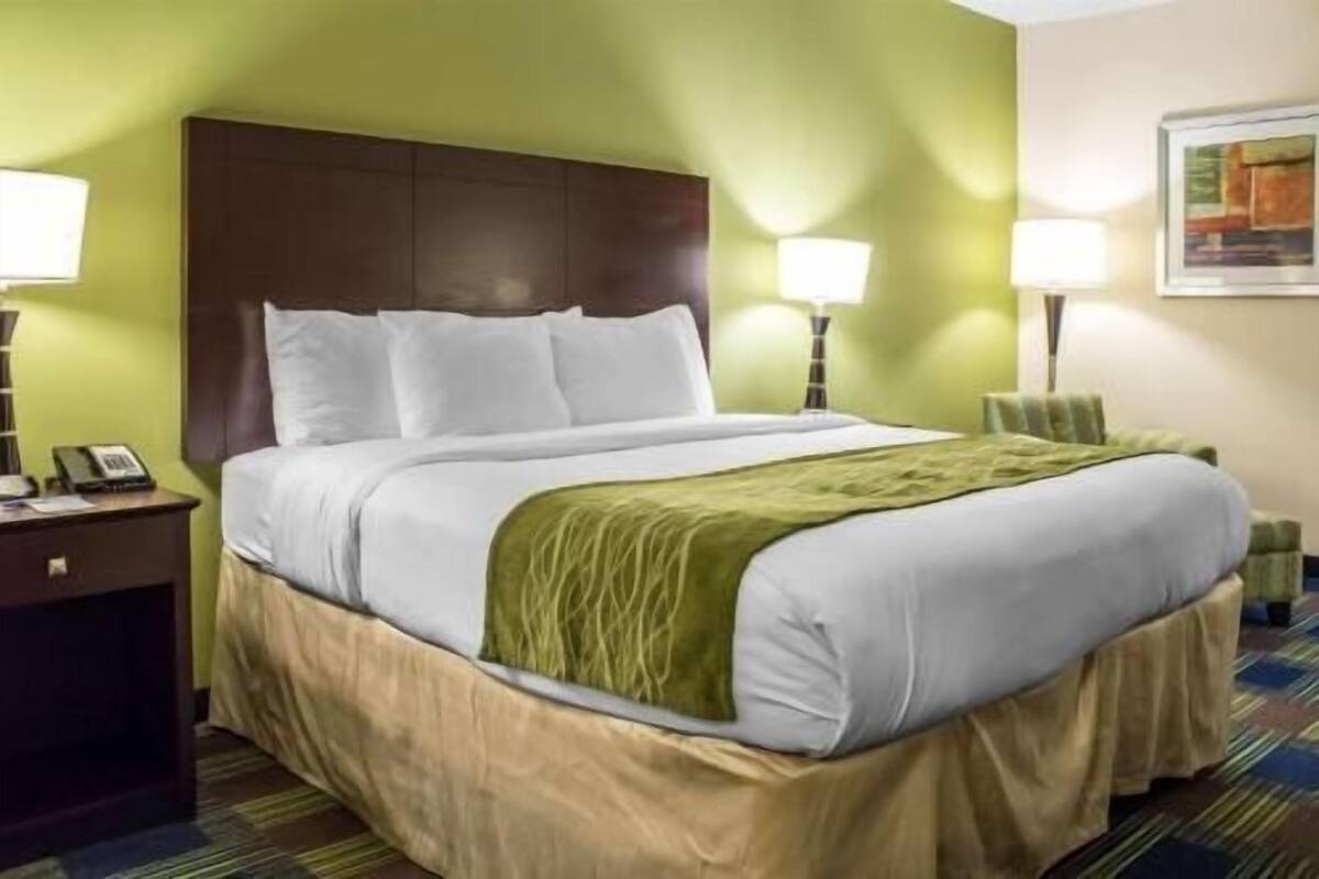 A hotel room with a bed, bedside lamps, a nightstand, and a painting on the wall.