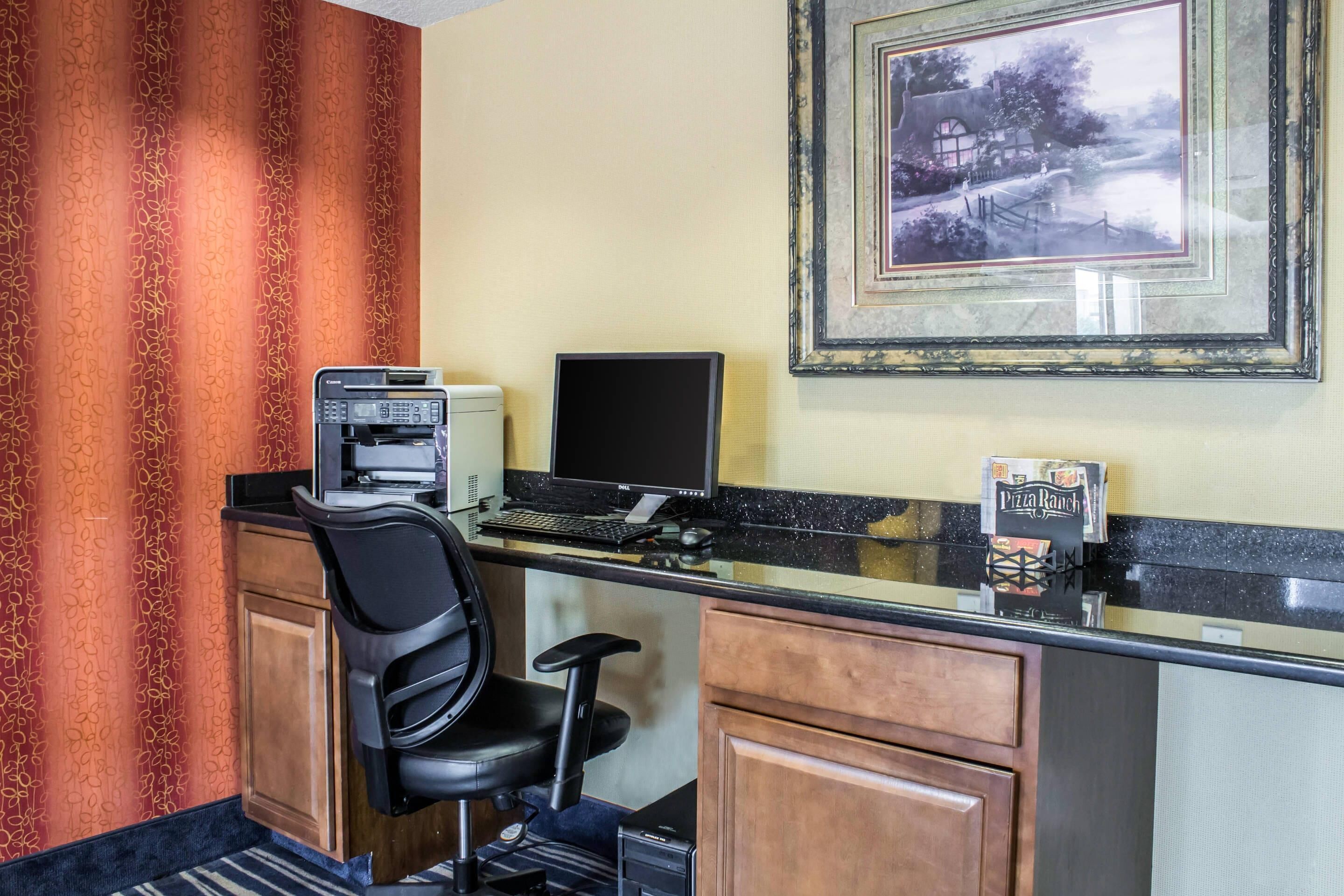 Een hotelkamer met een bureau, computer, stoel en een lijst aan de muur.
