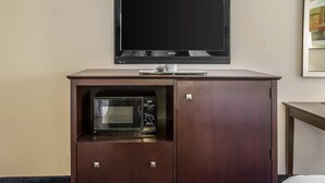A television mounted on a wall above a wooden cabinet with a microwave inside. - Econo Lodge Ankeny - Des Moines (Ankeny)