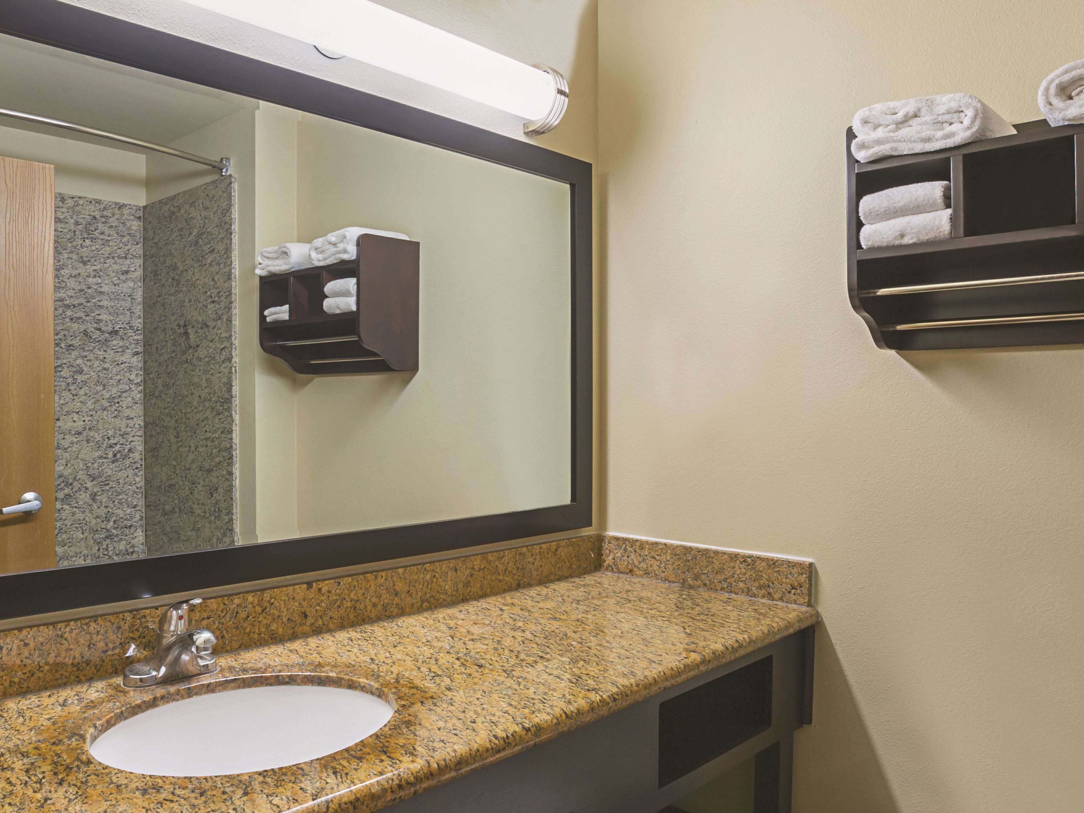 A bathroom with a granite countertop sink, a large mirror, and a towel rack with folded towels.
