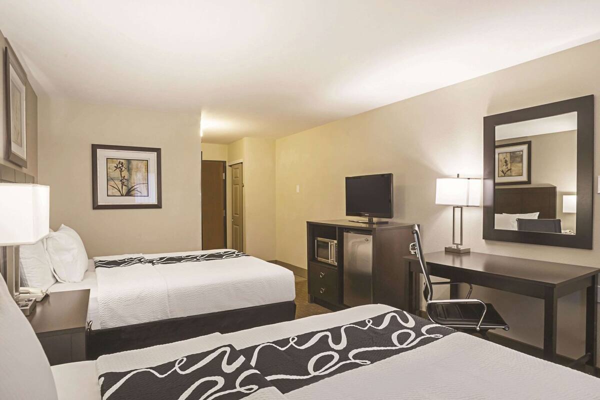 Een hotelkamer met twee bedden, een bureau met een televisie, een spiegel en een deur naar een andere kamer.
